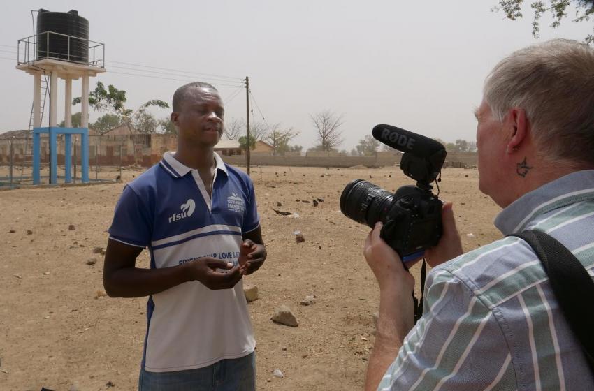 Clement Akazeire Nyaaba, head teacher of Foe Primary School B, being interviewed in front of water tower that serves schools in the town