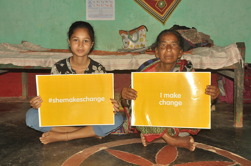 Young woman holding &quot;#shemakeschange&quot; card sitting next to old woman holding &quot;#I make change&quot;, Odisha, India